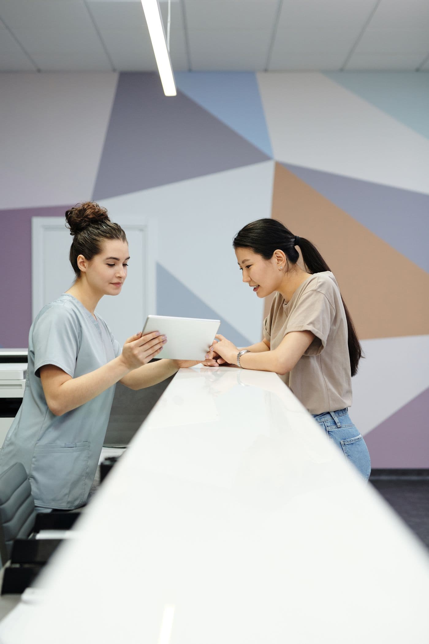 Clinic receptionist reviewing information on a tablet with a visitor